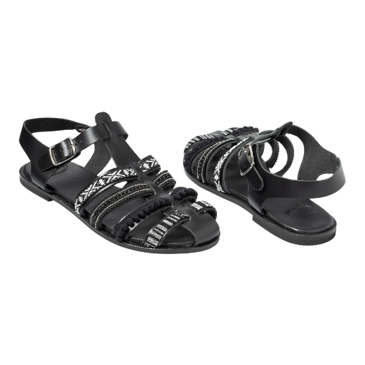 A black sandal featuring multiple straps with various textures and patterns, including a buckle strap around the ankle and decorative details on the upper straps.