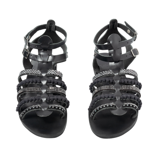 A black sandal with double buckle straps around the ankle and several upper straps adorned with different textures and embellishments.