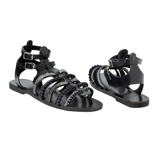 A black sandal with double buckle straps around the ankle and several upper straps adorned with different textures and embellishments.