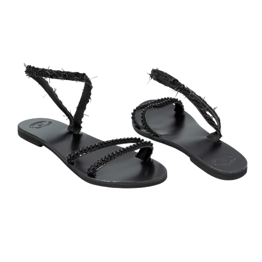 A black sandal with a single textured strap wrapping around the ankle and two thin upper straps, all featuring small decorative elements.