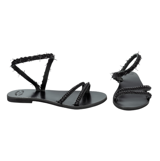 A black sandal with a single textured strap wrapping around the ankle and two thin upper straps, all featuring small decorative elements.