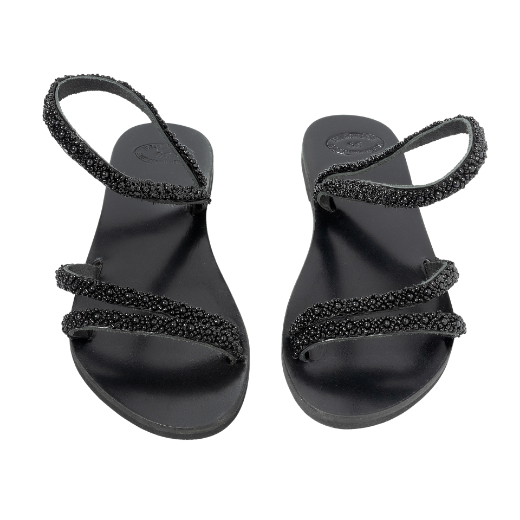 A black sandal with a single looped strap around the ankle and two thin upper straps, embellished with small decorative elements.