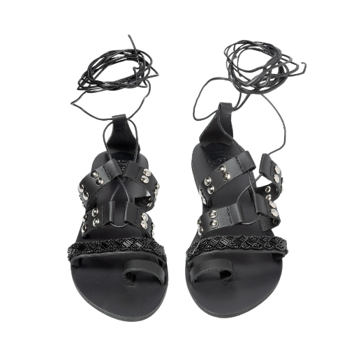 A black sandal with a lace-up design, featuring multiple straps with studs and textured details on the upper foot and a toe loop.