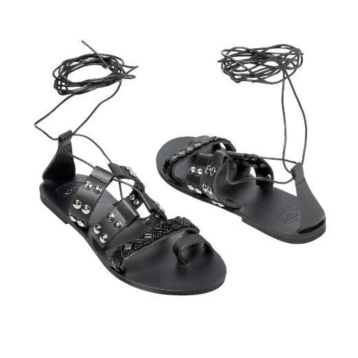 A black sandal with a lace-up design, featuring multiple straps with studs and textured details on the upper foot and a toe loop.